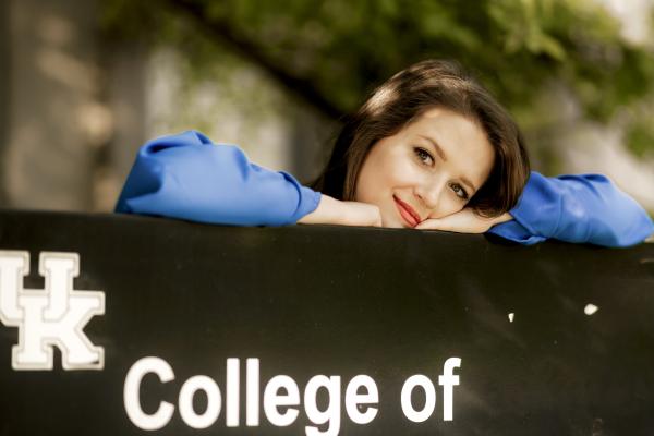 a photograph of Sarah Jane Robbins resting their head on a sign for the College of Public Health