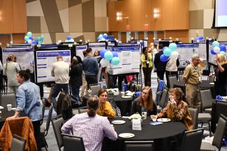 a photograph of people eating and socializing at tables, with poster presentations in the background