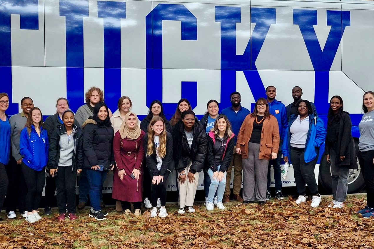 a photograph of a group of University of Kentucky (UK) College of Public Health students and faculty standing in front of UK bus