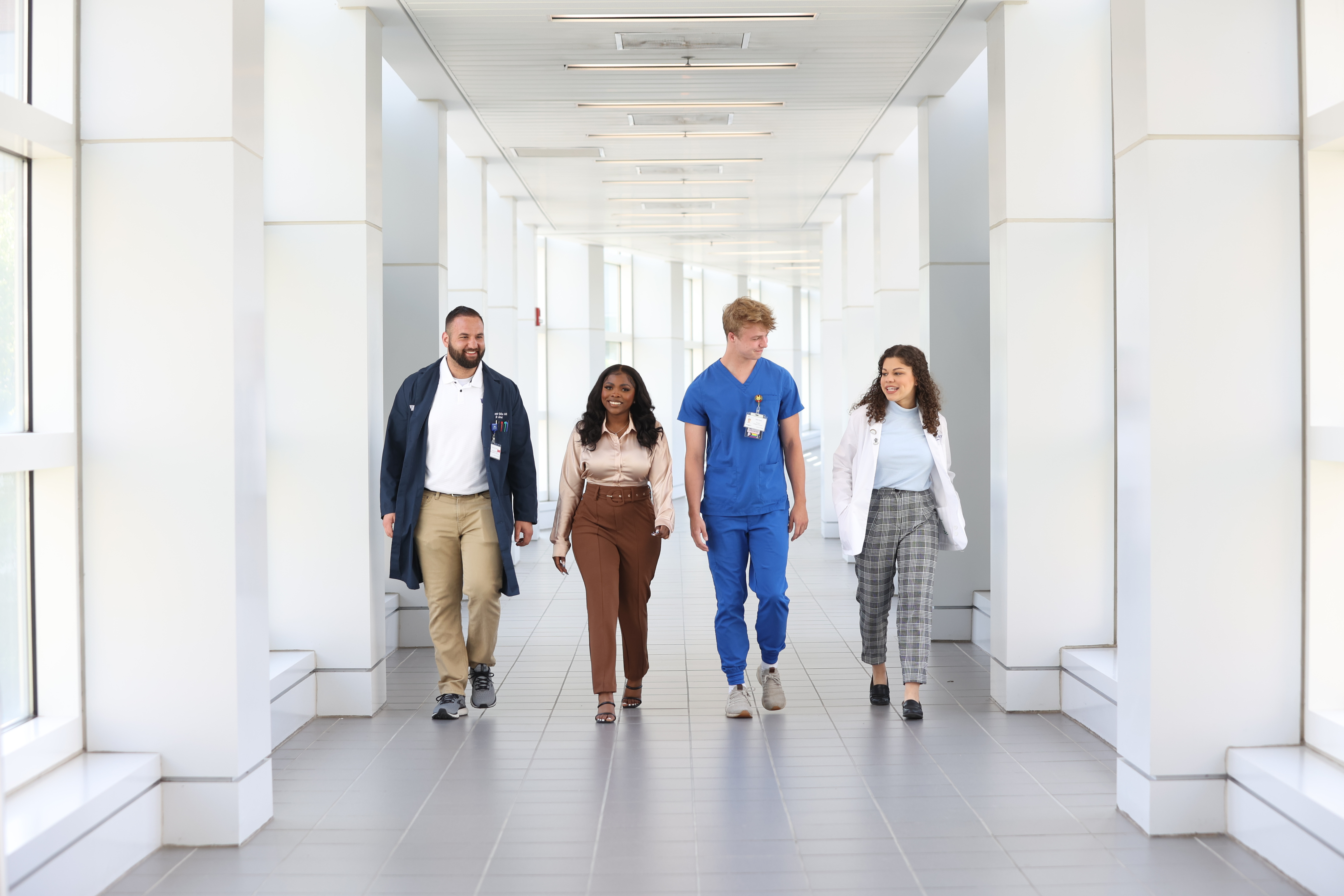 Four students representing medicine, public health, nursing and health science walking down a corridor.