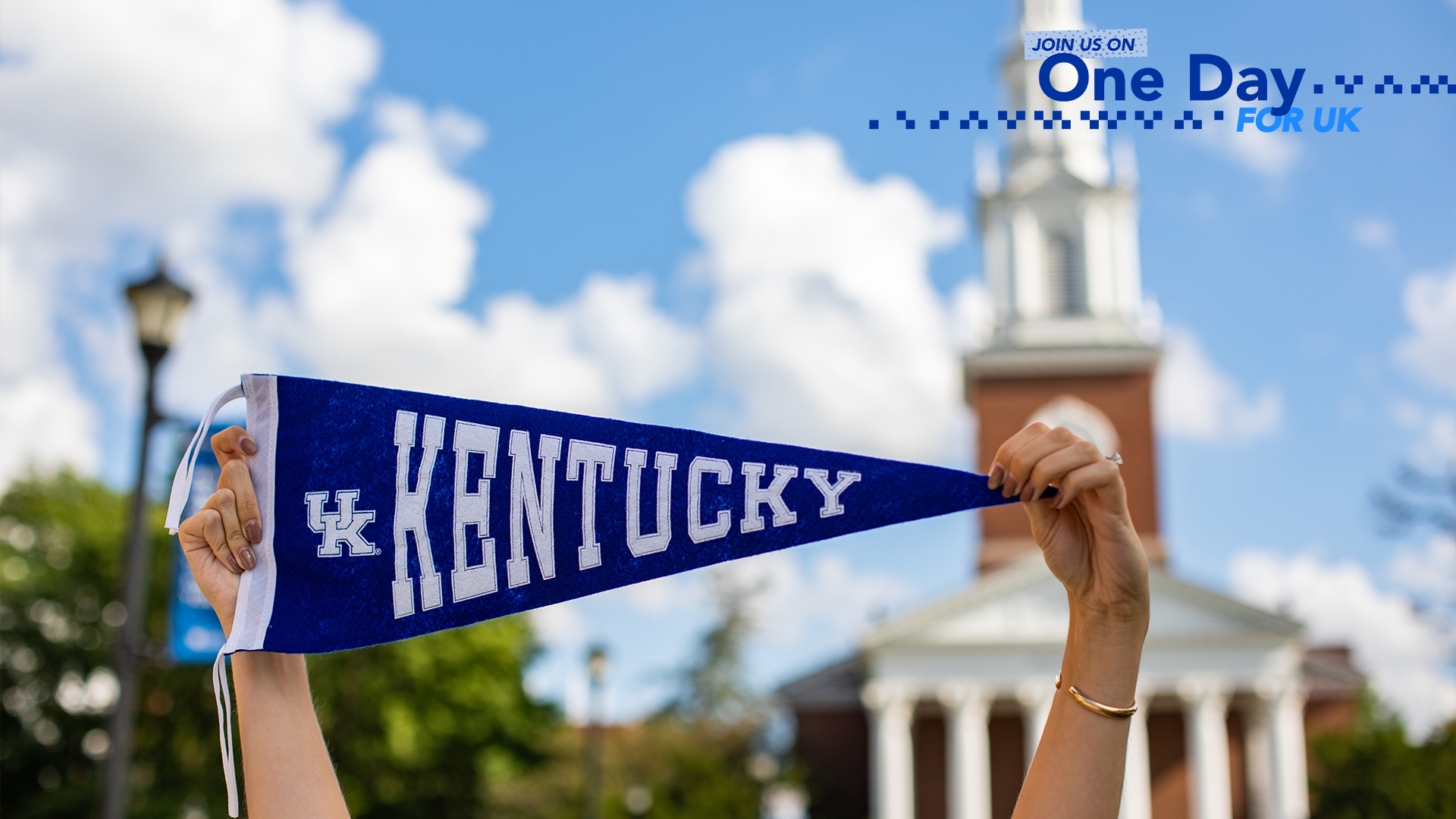 a photograph of hands holding up a University of Kentucky school flag