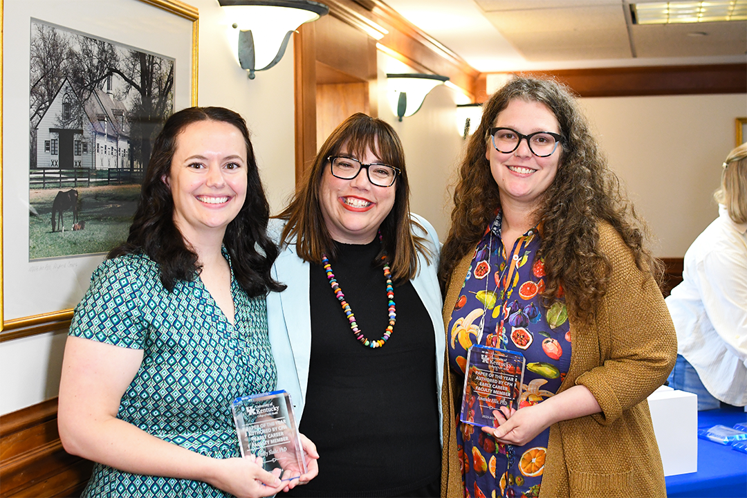 a photograph of Amanda Ellis and Caitlin Northcutt holding their awards on either side of Heather Bush