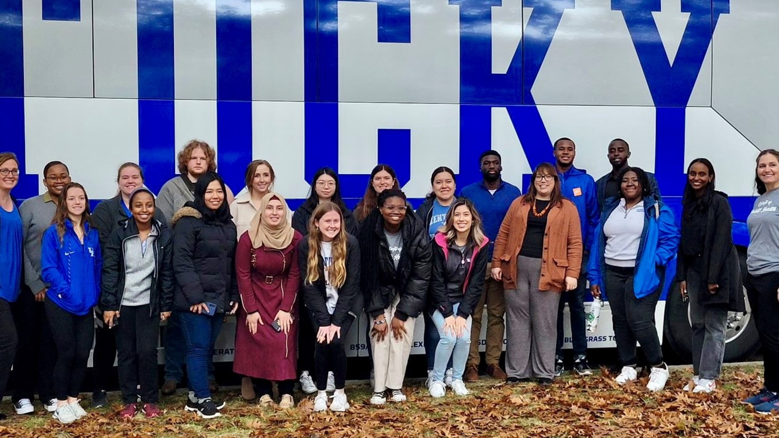 a photograph of a group of University of Kentucky (UK) College of Public Health students and faculty standing in front of UK bus