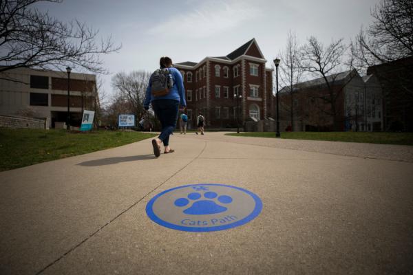 a photograph of a student walking along one of University of Kentucky's pathways where a blue cat footprint is imprinted on the concrete