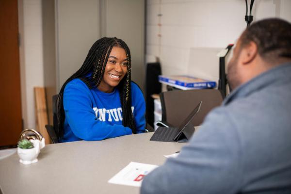 a student in a blue University of Kentucky sweatshirt sits across from a UK staff member