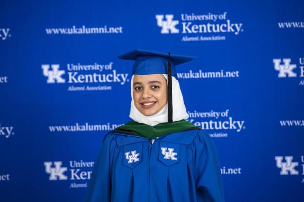 a photograph of a University of Kentucky student in the graduation robes in front of a UK backdrop