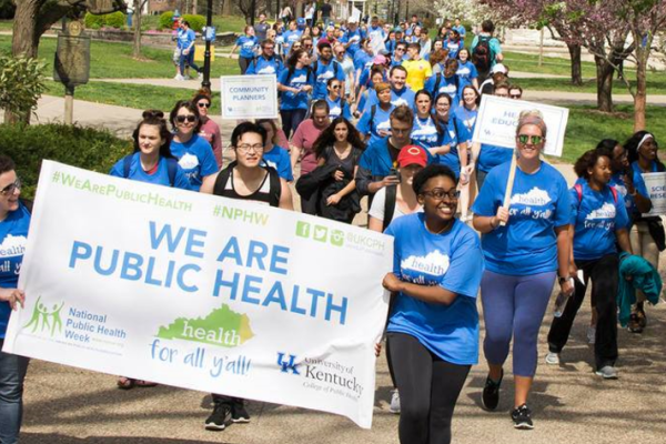 a photograph of students marching on campus in College of Public Health blue shirts and holding a sign stating "we are public health"
