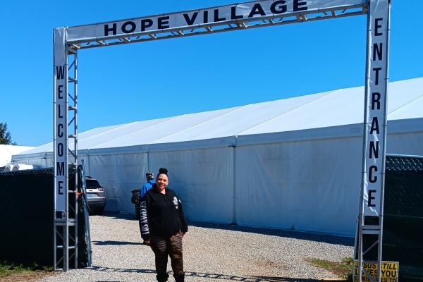 a photograph of a person standing below a gate reading "hope village"