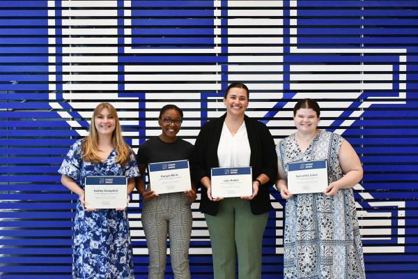 a photograph of Ashley Grospitch, Kangai Miriti, Julia Kollitz, and Samantha Jones holding their student awards certificates