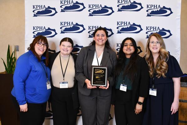 a photograph of Heather Bush, Anna Hallahan, and three other students at the KPHA event posing with their award