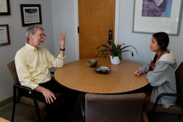 a photograph of John Lyons being interviewed at a desk in an office