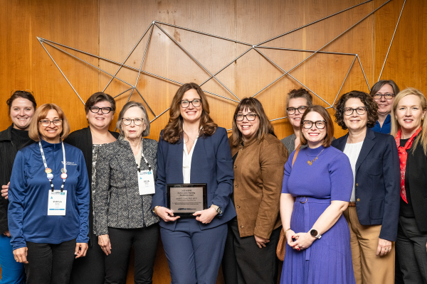 a photograph of Sarah Cprek posing for the camera with her reward surrounded by other faculty members