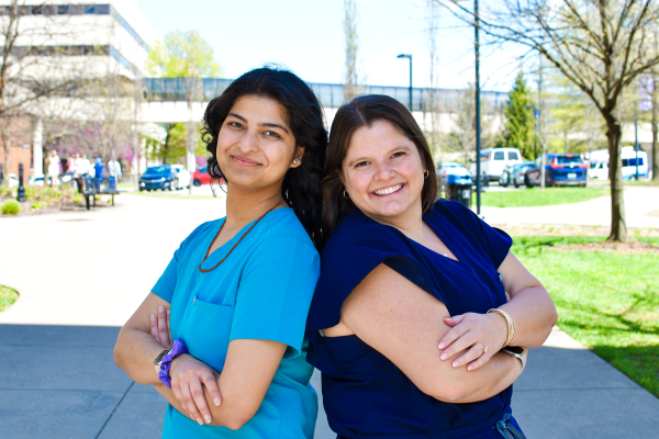 A photograph of Riya Patel and Grace Bush standing back to back on the medical campus of the University of Kentucky