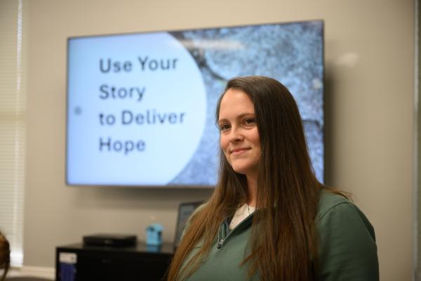 a photograph of Brook West in front of a PowerPoint that says "use your story to deliver hope"