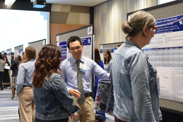 a photograph of a student talking about their research poster while pointing at it