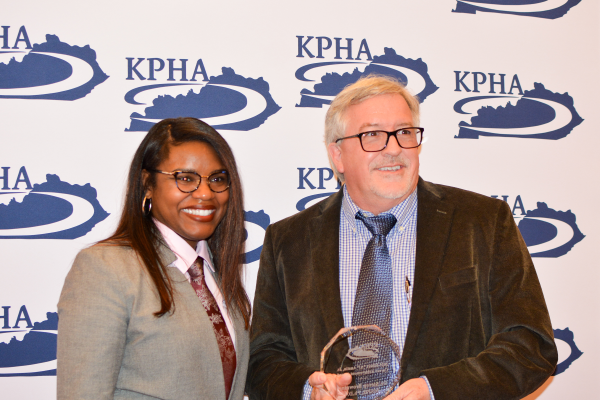 Dr. Steve Browning standing next to KPHA President in front of a KPHA backdrop while holding the Elbert “Al” Austin Career Achievement Award  