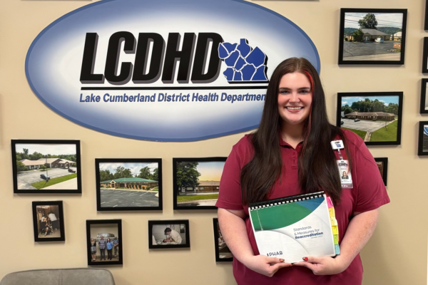 a photograph of Karcyn Brummett posing in front of the Lake Cumberland District Health Department sign