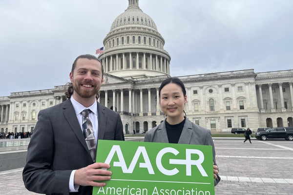 a photograph of two people standing in front of the U.S. Capitol building holding an AACR sign, with Subin Kim on the right
