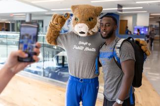 a photograph of The Wildcat mascot posing with current College of Public Health student Christopher Otieno