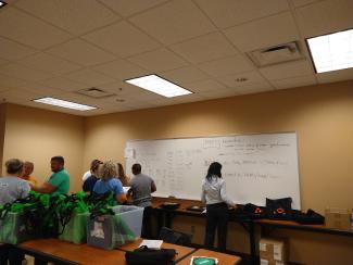 a photograph of flood aid workers in a conference room with a whiteboard with written instructions for them on it