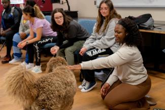 a photograph of students in a classroom petting a dog