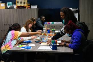 a photograph of students drawing using art supplies on a table