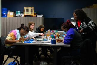 a photograph of students drawing on a table with art supplies