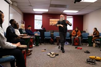 a photograph of students drumming in a classroom lead by Austin Robinson