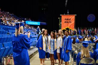 Students pictured in graduation regalia in front of the public health flag