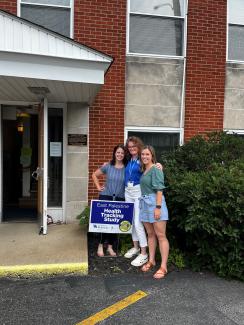 Dr. Haynes outside of a building with two students in front of a sign reading "East Palestine health tracking study"