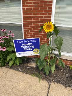 a sign planted next to a sunflower reading "East Palestine health tracking study"