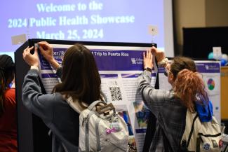a photograph of two students pinning a research poster up together