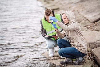 a stock photograph of a woman filling a beaker next to a river