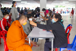 a photograph of a vaccination clinic in Taiwan with a monk getting their temperature read
