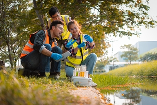a stock photograph of three people in high visibility vests examining a vial filled with the water of the river they are next to