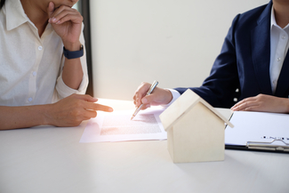 a stock photograph of two people going over a document with a model house in front of them
