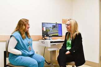  A University of Kentucky College of Public Health student in blue scrubs and a professional staff member smile and talk together in a clinical office setting.
