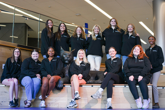 A group of 13 Public Health student ambassadors all wearing black sweatshirts with the UK logo on them in front of the gatton student center's bowman statue