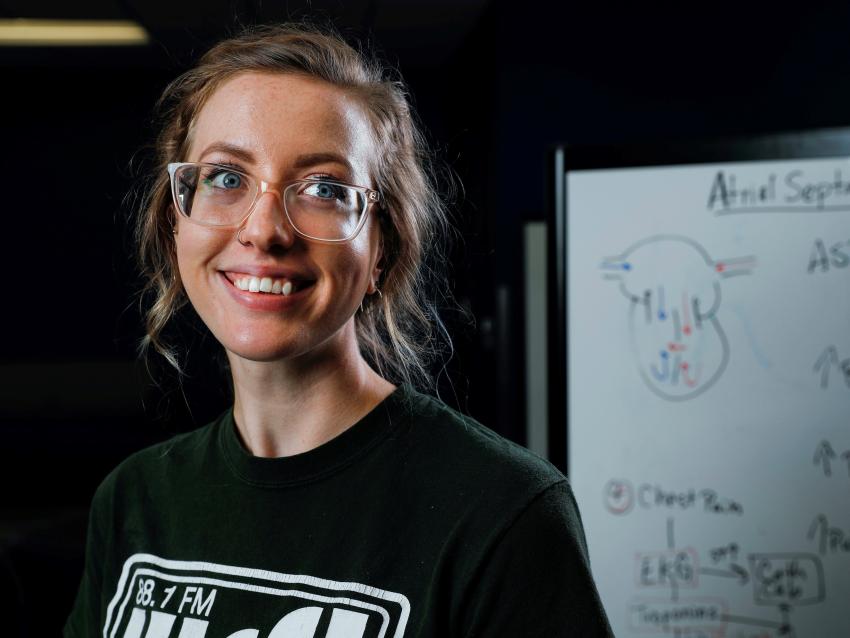 a photograph of a student smiling at the camera with a whiteboard in the background