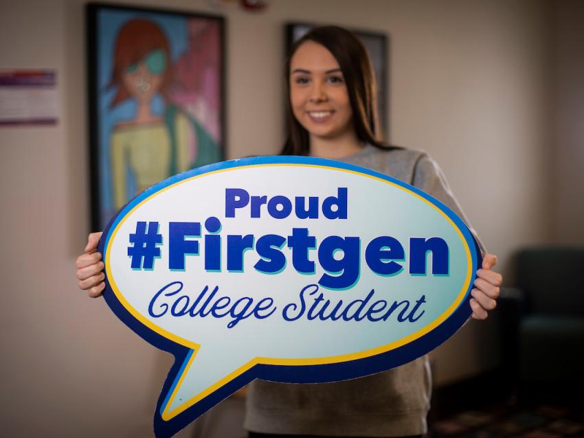 a photograph of a student holding a sign shaped like a talk bubble stating "proud #firstgen college student"