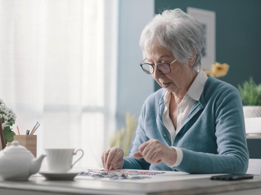 a photograph of a senior woman sitting at desk and solving a puzzle