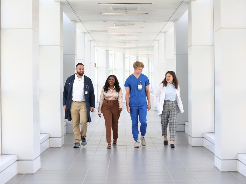 Four students representing medicine, public health, nursing and health science walking down a corridor.