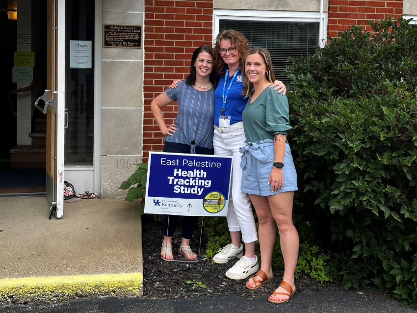 a photograph of Dr. Erin Haynes and two students in front a lawn sign that reads "East Palestine health tracking study"