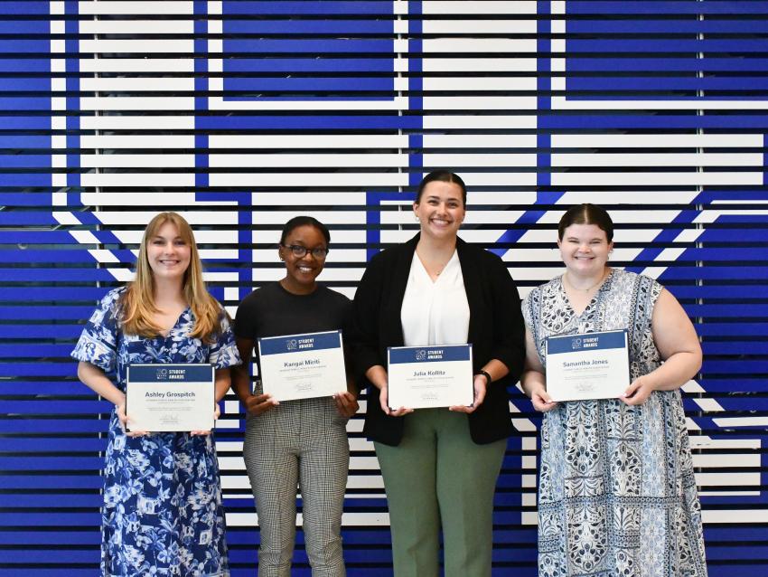 a photograph of Ashley Grospitch, Kangai Miriti, Julia Kollitz, and Samantha Jones holding their student awards certificates