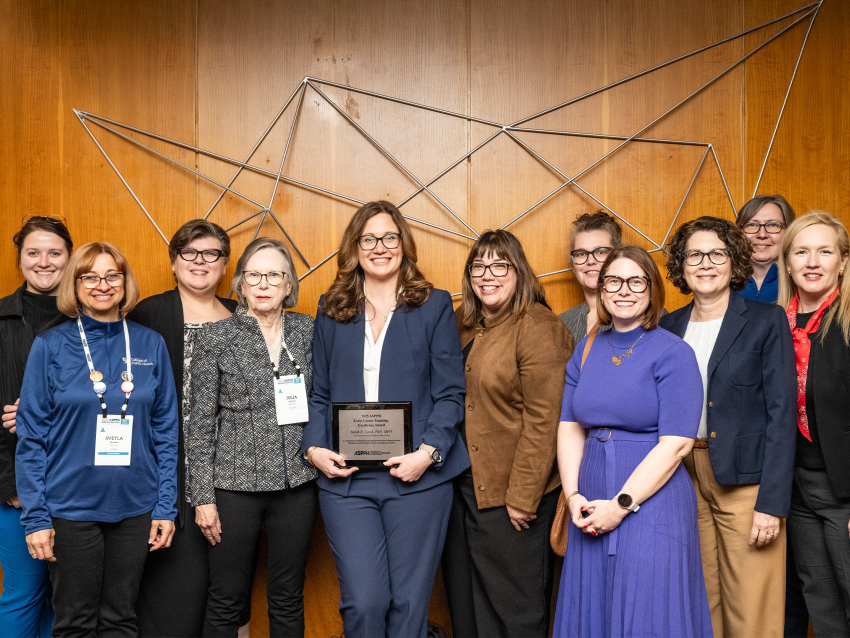 a photograph of Sarah Cprek posing for the camera with her reward surrounded by other faculty members