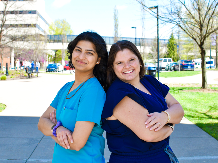 A photograph of Riya Patel and Grace Bush standing back to back on the medical campus of the University of Kentucky