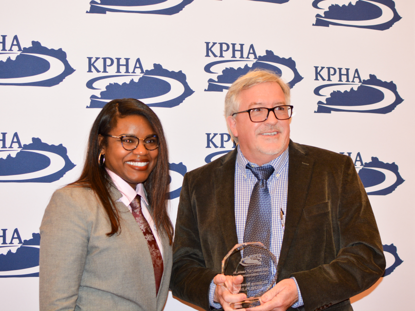 Dr. Steve Browning standing next to KPHA President in front of a KPHA backdrop while holding the Elbert “Al” Austin Career Achievement Award  