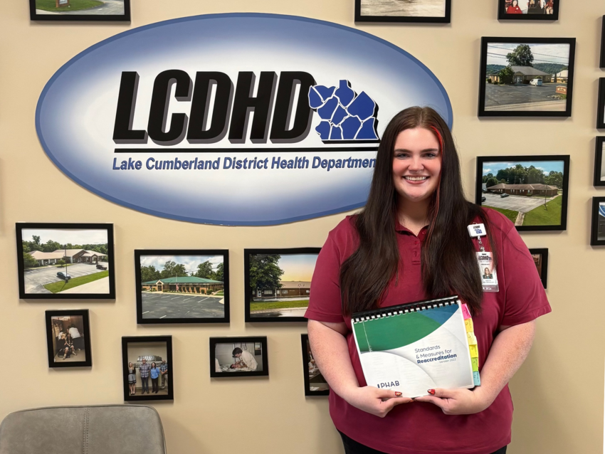 a photograph of Karcyn Brummett posing in front of the Lake Cumberland District Health Department sign