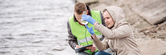 a stock photograph of a woman filling a beaker next to a river